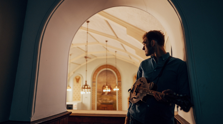 Photo of Musician holding a mandolin and posing in a doorway.