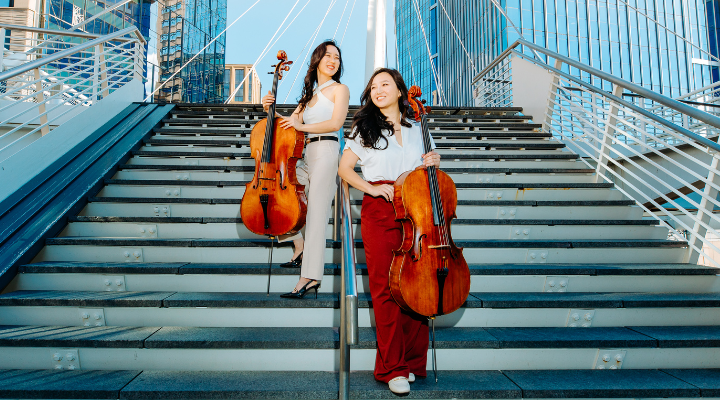 Two female musicians posing outside in Denver, holding their cellos.